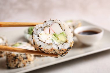 Chopsticks with tasty sushi roll, closeup view clipart