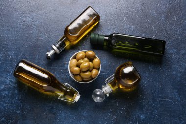 Olgun zeytinlerle dolu bir kase ve mavi arka planda bir şişe yağ.