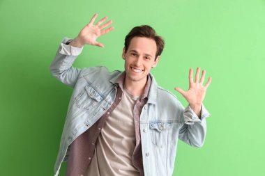 Yeşil arka planda ellerini gösteren genç adam.