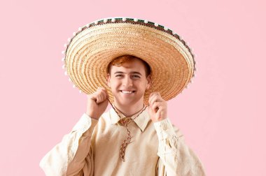 Pembe arka planda şapkalı Meksikalı genç bir adamın portresi.