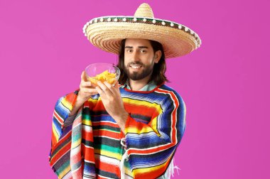 Sombrero, panço ve mor arka planda nachos giyen yakışıklı Meksikalı genç adam.