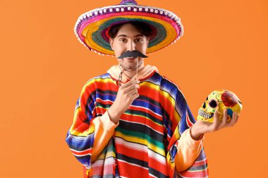 Turuncu arka planda boyalı kafatası ve kağıt bıyıklı yakışıklı bir Meksikalı. Ölüler Günü Kutlaması