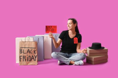 Alışveriş torbaları, karton kutular ve mor arka planda oturan genç bir kadın. Kara Cuma indirimi