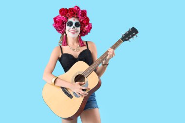 Kafatası boyalı genç bir kadın mavi arka planda gitar çalıyor. Meksika Ölüler Günü (El Dia de Muertos) kutlamaları