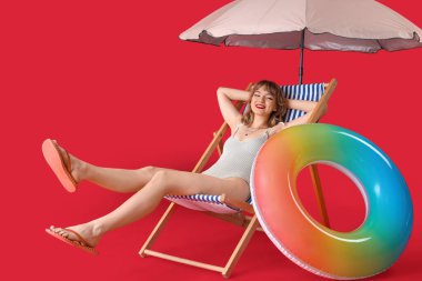 Kumsal şemsiyeli ve kırmızı arka planda yüzen genç bir kadın.