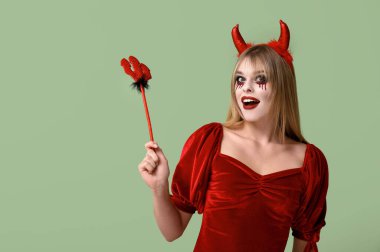 Young woman dressed for Halloween as devil with trident on green background clipart