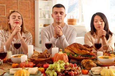 Şükran Günü 'nde şenlik masasında dua eden bir grup genç arkadaş.