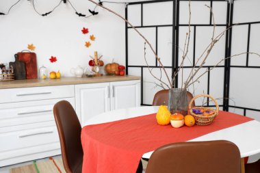 Dining table with vase, Halloween pumpkins and candies in festive kitchen clipart