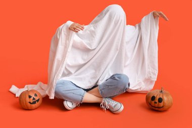 Cadılar Bayramı kostümlü kadın balkabaklı hayalet renkli arka planda oturuyor.