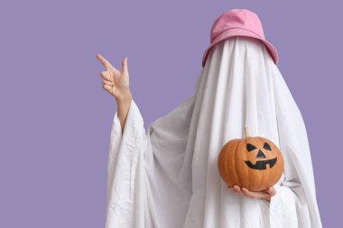 Cadılar Bayramı kostümlü kadın ve balkabaklı şapka leylak arka plandaki bir şeyi işaret ediyor.