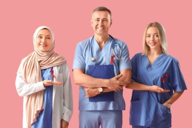 Pembe arka planda kırmızı kurdeleli profesyonel doktor ekibi. Dünya AIDS Günü konsepti
