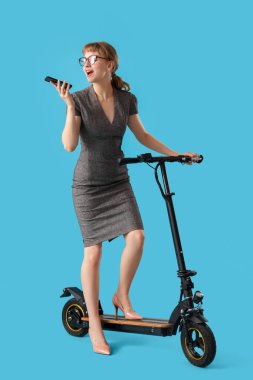 Tekme scooterlı genç iş kadınının portresi mavi arka planda telefonla konuşuyor.