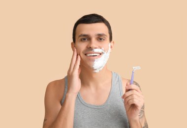 Yüzünde jilet ve tıraş köpüğü olan yakışıklı genç bir adam.