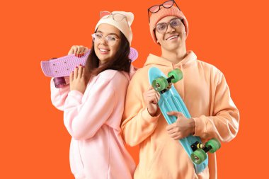 Turuncu arka planda kaykay yapan gözlüklü genç bir çift.