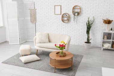 Beyaz şık oturma odasının içinde kanepe, çiçekli vazo, sehpa ve raf ünitesi var.