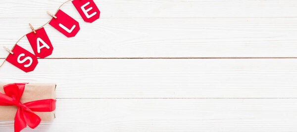 Гирлянда со словом ПРОДАЖА и подарок на белом деревянном фоне с пространством для текста