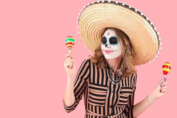 stock image Young woman with painted skull and maracas on pink background. Mexico's Day of the Dead (El Dia de Muertos) celebration