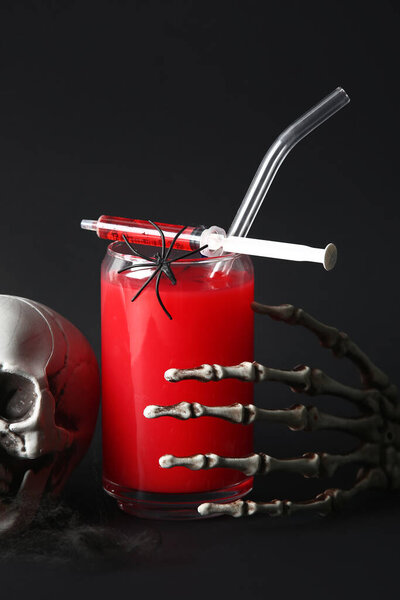 Glass of delicious red cocktail, skeleton hand, skull and syringe for Halloween celebration on black background, closeup