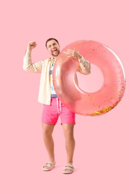 Pembe arka planda şişme yüzüğü olan neşeli genç bir adamın portresi.