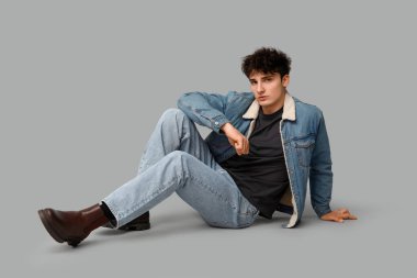 Gri arka planda oturan şık elbiseli yakışıklı genç adam.