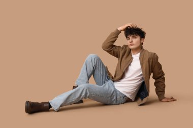 Kahverengi arka planda oturan şık elbiseli yakışıklı genç adam.