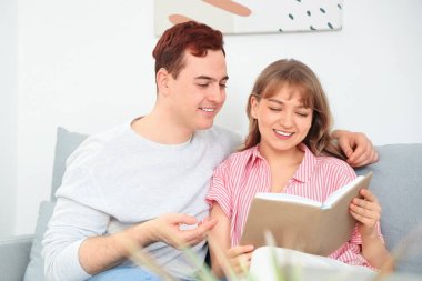 İşitme cihazı olan genç bir adam ve kız arkadaşı evdeki kanepede kitap okuyorlar.