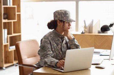 Female African-American soldier working with computer at table in headquarters clipart