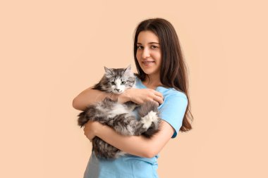 Bej arka planda uzun saçlı sevimli bir kedi tutan genç kadın.