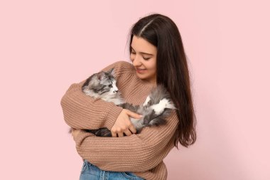 Pembe arka planda uzun saçlı sevimli kedisi olan genç bir kadın.