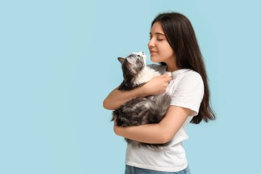 Mavi arka planda uzun saçlı sevimli bir kedi tutan genç kadın.
