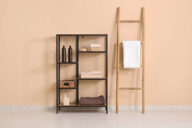 Bej duvarın yanında havlu ve banyo aksesuarlarıyla raf ünitesi.