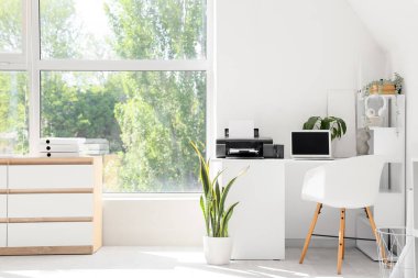 Laptop, yazıcı ve bitkilerin bulunduğu modern işyeri