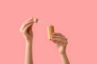 Female hands with bottle of cosmetic product on pink background