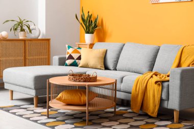 Güzel oturma odasının içinde rahat bir kanepe, çiçekler, yastıklar ve kahve masası.