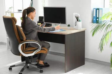 Koltukta oturan ve işyerinde cep telefonu kullanan kadın ofis çalışanı.