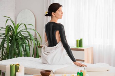 Çamurlu genç bir kadın kaplıcada oturuyor.