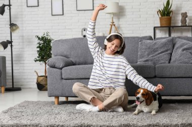 Kulaklıklı, sevimli bir Beagle köpeği olan genç bir kadın evdeki kanepenin yanında oturuyor.