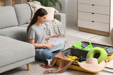 Genç bir kadın harita öğreniyor ve evde bavulunu topluyor. Yaz yolculuğu konsepti