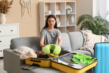 Evdeki kanepede yastığı valize koyan genç bir kadın. Yaz yolculuğu konsepti