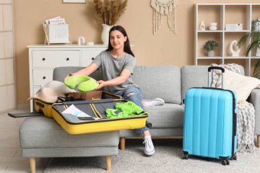 Evdeki kanepede yastığı valize koyan genç bir kadın. Yaz yolculuğu konsepti