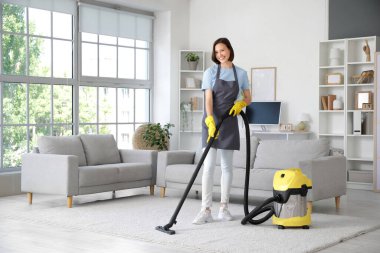 Kadın hademe odada halı temizliyor.