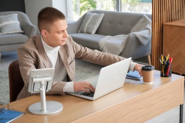 Modern ev ofisinde dizüstü bilgisayarla çalışan genç bir serbest çalışan.