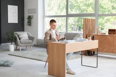 Modern ev ofisinde tablet bilgisayarla çalışan genç bir serbest çalışan erkek.