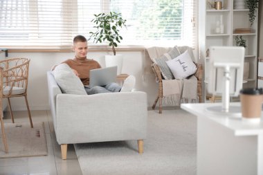 Ev ofisteki kanepede oturan dizüstü bilgisayarlı genç bir serbest çalışan.