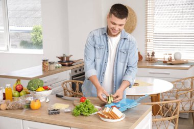 Genç adam mutfakta beslenme çantası için sebze kesiyor.