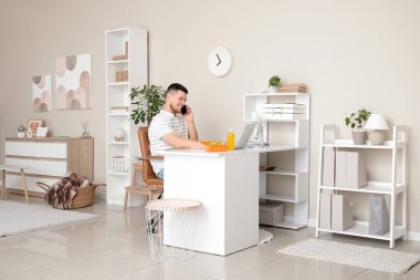 Bilgisayarlı ve beslenme çantalı genç adam telefonda konuşuyor.