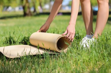 Genç bir kadın parkta yeşil çimlere yoga minderi yerleştiriyor.