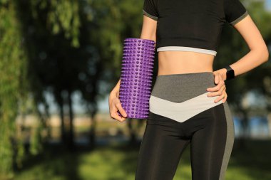 Parkta köpük silindirli ve spor takip cihazlı genç bir kadın, yakın plan.