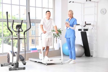 Rehabilitasyon merkezinde koşu bandında genç bir adamla çalışan kadın fizyoterapist.