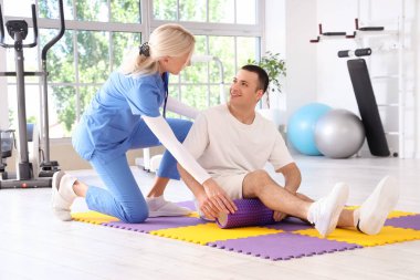 Kadın fizyoterapist ve rehabilitasyon merkezinde köpük paten eğitimi almış genç bir adam.